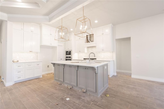 kitchen with light wood finished floors, gray cabinets, built in microwave, light countertops, and stainless steel oven