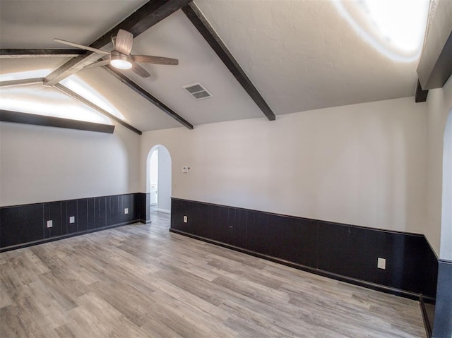 empty room featuring wood walls, lofted ceiling with beams, ceiling fan, and light wood-type flooring