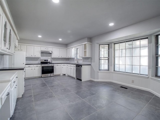 kitchen with sink, decorative backsplash, dark tile patterned floors, appliances with stainless steel finishes, and white cabinetry