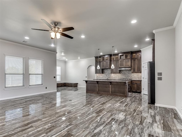 kitchen with dark brown cabinetry, decorative light fixtures, a kitchen island with sink, and ornamental molding