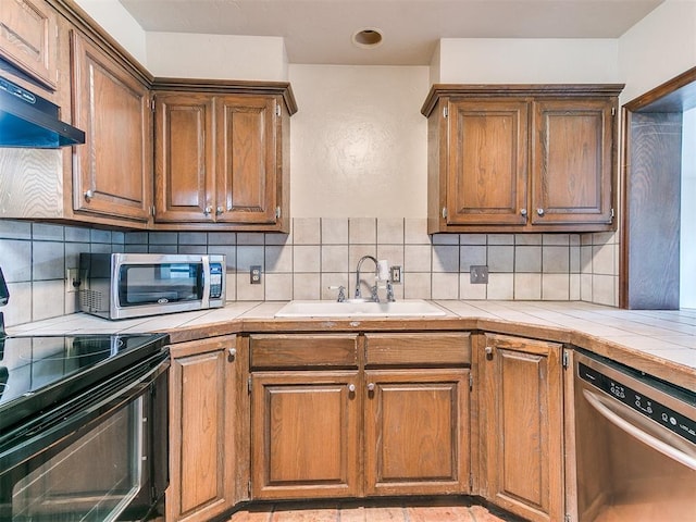 kitchen with tile counters, sink, decorative backsplash, and stainless steel appliances