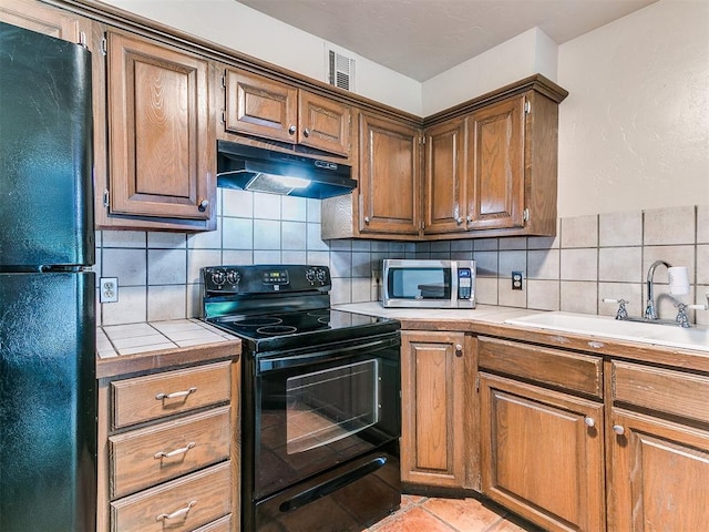 kitchen with tasteful backsplash, sink, black appliances, light tile patterned floors, and tile counters