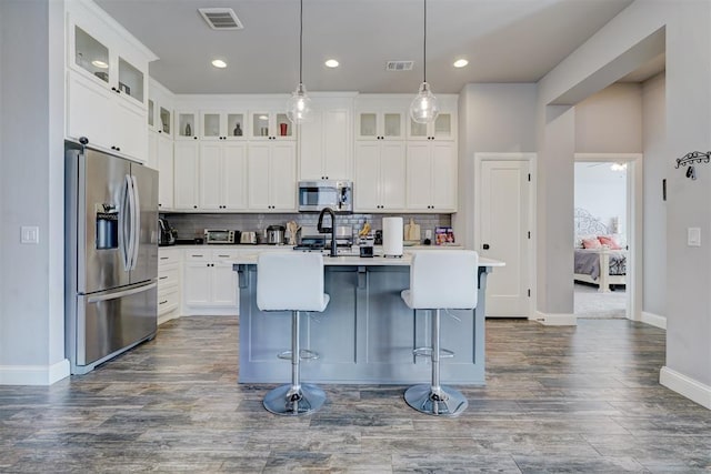 kitchen with an island with sink, decorative light fixtures, a breakfast bar, white cabinets, and appliances with stainless steel finishes