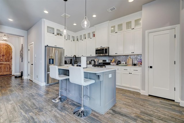 kitchen featuring hanging light fixtures, stainless steel appliances, white cabinets, and a kitchen island with sink