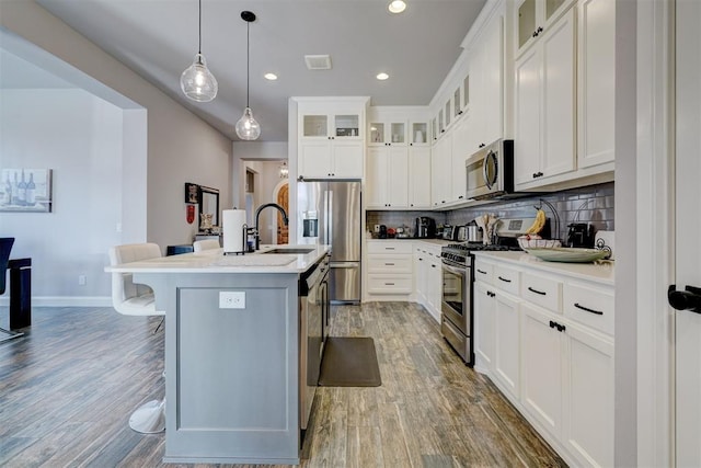 kitchen featuring backsplash, a kitchen island with sink, a kitchen bar, wood-type flooring, and stainless steel appliances