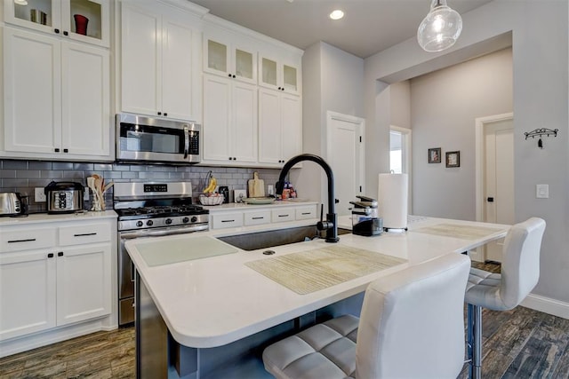 kitchen with sink, dark wood-type flooring, an island with sink, pendant lighting, and appliances with stainless steel finishes