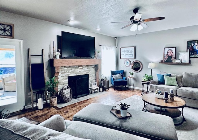 living room with hardwood / wood-style floors, a textured ceiling, a stone fireplace, and ceiling fan