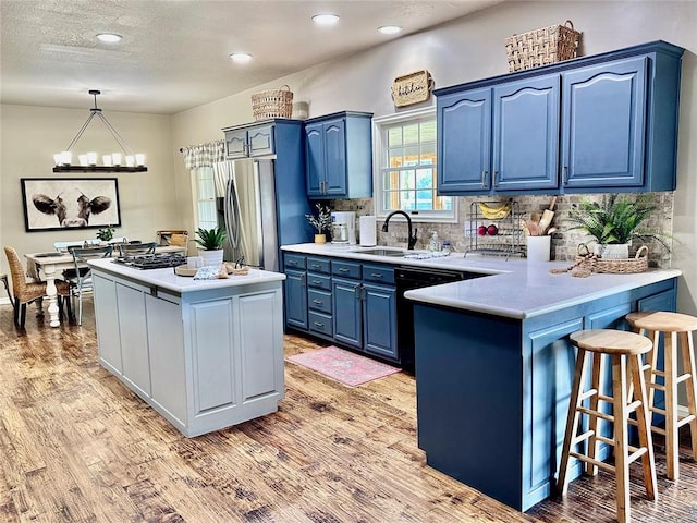 kitchen featuring kitchen peninsula, stainless steel appliances, sink, blue cabinetry, and hanging light fixtures