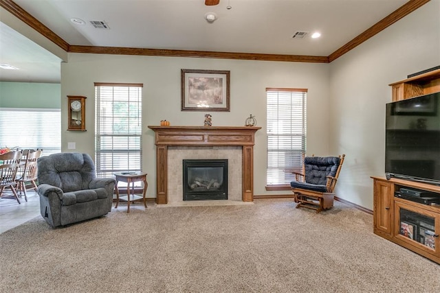 carpeted living room featuring a tiled fireplace, crown molding, and ceiling fan