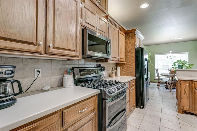 kitchen featuring pendant lighting, backsplash, an inviting chandelier, light tile patterned flooring, and stainless steel appliances