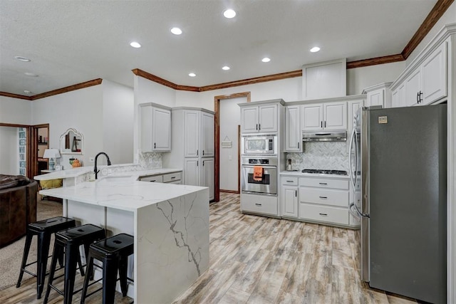 kitchen featuring sink, a kitchen breakfast bar, kitchen peninsula, appliances with stainless steel finishes, and light wood-type flooring