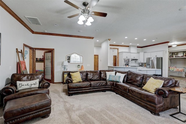 living room with a textured ceiling, ceiling fan, crown molding, and light carpet