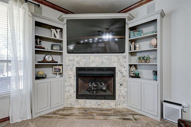 carpeted living room with a textured ceiling, built in features, crown molding, and a tiled fireplace