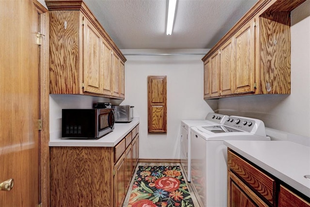 clothes washing area with washing machine and clothes dryer, cabinets, and a textured ceiling