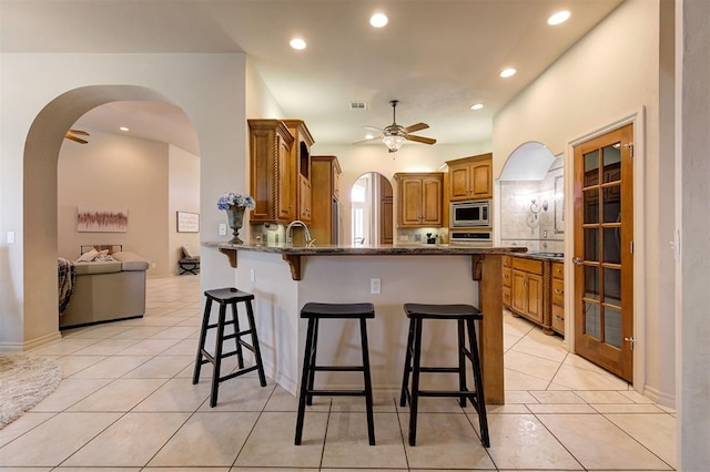 kitchen with kitchen peninsula, dark stone countertops, a breakfast bar area, light tile patterned floors, and appliances with stainless steel finishes