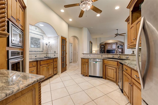 kitchen with decorative backsplash, light stone counters, stainless steel appliances, ceiling fan, and sink