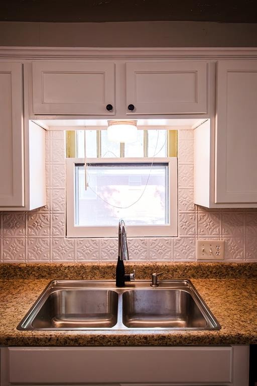 room details featuring backsplash, white cabinetry, sink, and dark stone counters