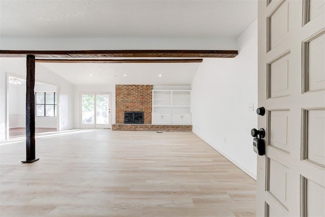 unfurnished living room featuring a fireplace, lofted ceiling with beams, and light hardwood / wood-style flooring