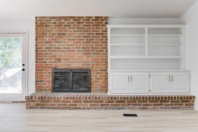 unfurnished living room featuring built in features, light hardwood / wood-style flooring, and a brick fireplace