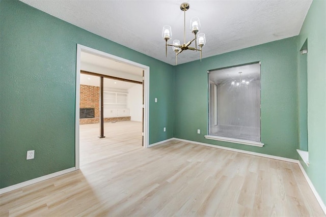 spare room with a chandelier, light hardwood / wood-style floors, a textured ceiling, and a brick fireplace