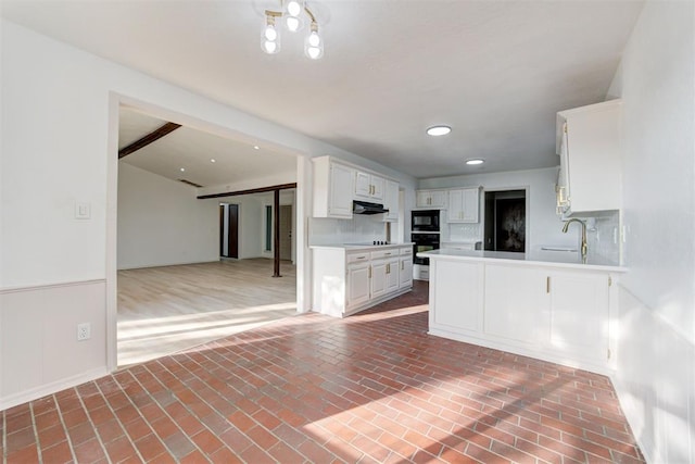 kitchen featuring white cabinetry, sink, backsplash, kitchen peninsula, and black appliances