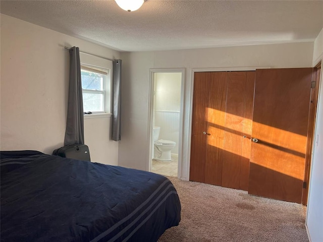 bedroom with connected bathroom, light carpet, and a textured ceiling