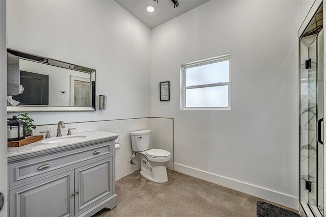 bathroom with vanity, toilet, a shower with shower door, and tile walls