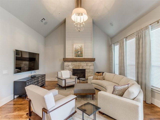 living room featuring light wood-type flooring, high vaulted ceiling, a stone fireplace, and a notable chandelier