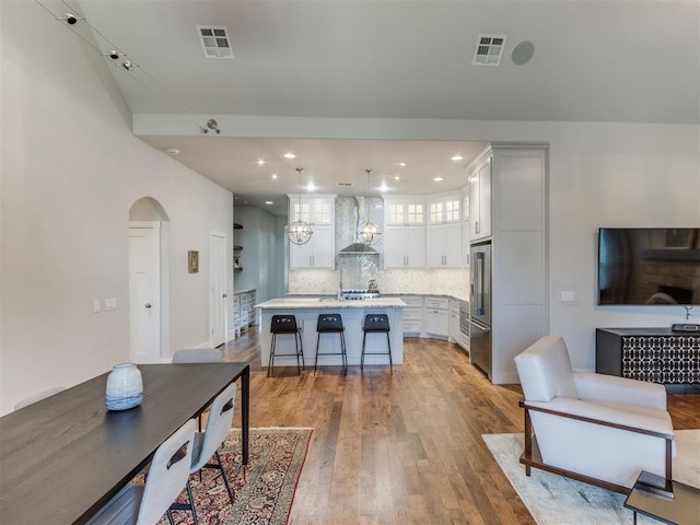 kitchen featuring hardwood / wood-style floors, a kitchen island with sink, white cabinets, wall chimney range hood, and a breakfast bar area