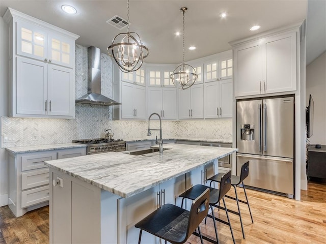 kitchen with sink, stainless steel appliances, wall chimney range hood, a notable chandelier, and a kitchen island with sink