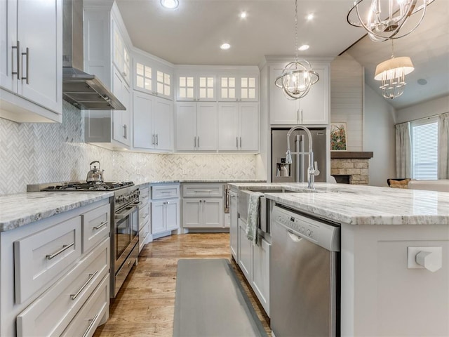 kitchen with white cabinetry, wall chimney exhaust hood, pendant lighting, a kitchen island with sink, and appliances with stainless steel finishes