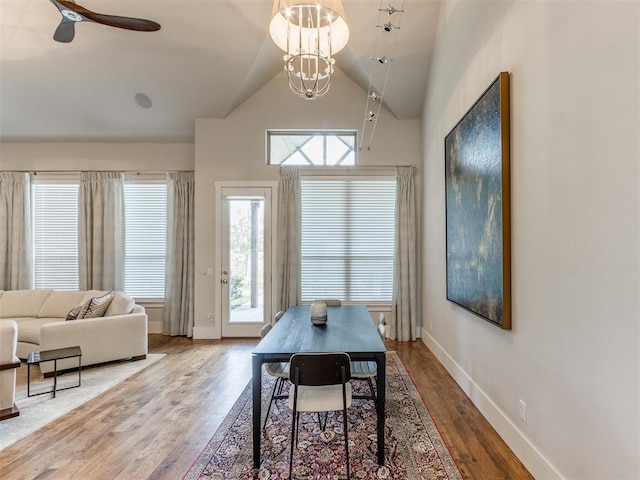 dining space with ceiling fan with notable chandelier, hardwood / wood-style flooring, and high vaulted ceiling