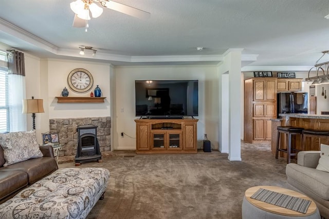 carpeted living room featuring a textured ceiling, ceiling fan, a wood stove, and ornamental molding