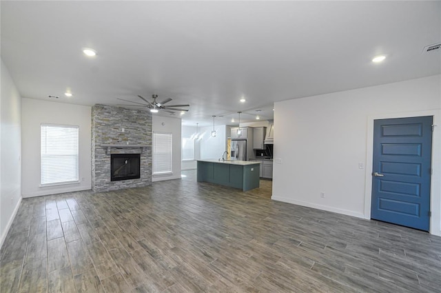 unfurnished living room featuring dark hardwood / wood-style floors, ceiling fan, a stone fireplace, and sink