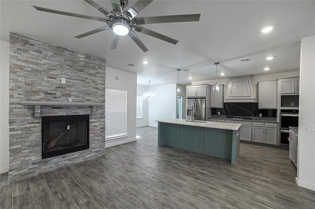 kitchen featuring dark hardwood / wood-style flooring, premium range hood, a kitchen island with sink, and stainless steel appliances