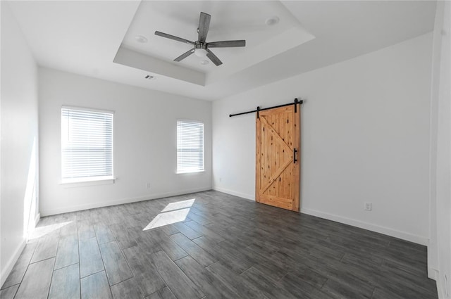 spare room with a raised ceiling, a barn door, ceiling fan, and dark wood-type flooring