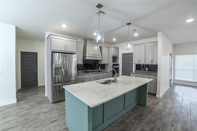 kitchen featuring a center island with sink, sink, gray cabinets, tasteful backsplash, and stainless steel appliances