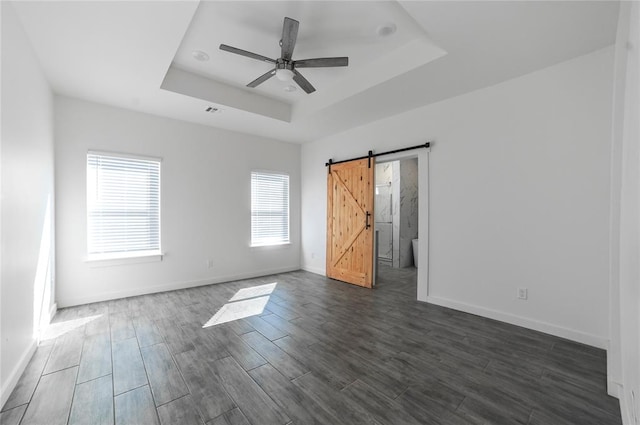 spare room featuring dark hardwood / wood-style flooring, a barn door, a tray ceiling, and ceiling fan