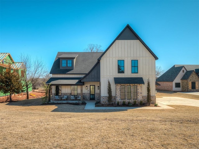 modern farmhouse featuring brick siding, board and batten siding, a shingled roof, a porch, and a front yard