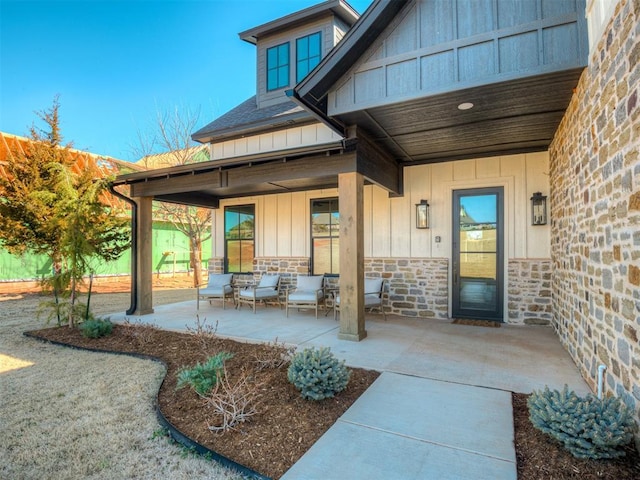 view of exterior entry featuring stone siding, board and batten siding, a shingled roof, and a patio area