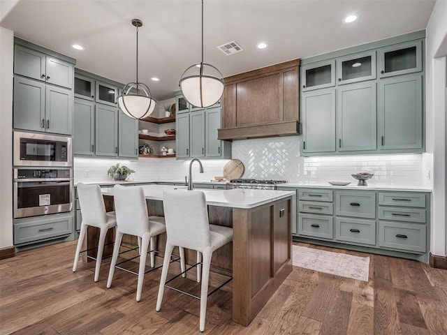 kitchen with visible vents, dark wood finished floors, an island with sink, stainless steel appliances, and light countertops