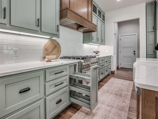 kitchen with glass insert cabinets, premium range hood, dark wood finished floors, light stone counters, and decorative backsplash