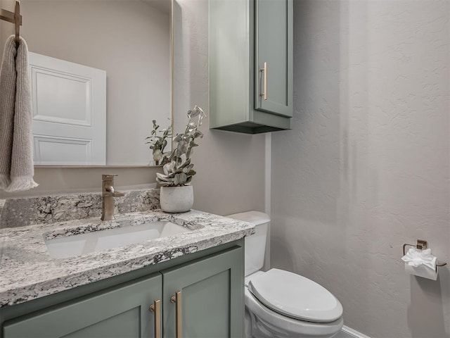 bathroom with toilet, vanity, and a textured wall