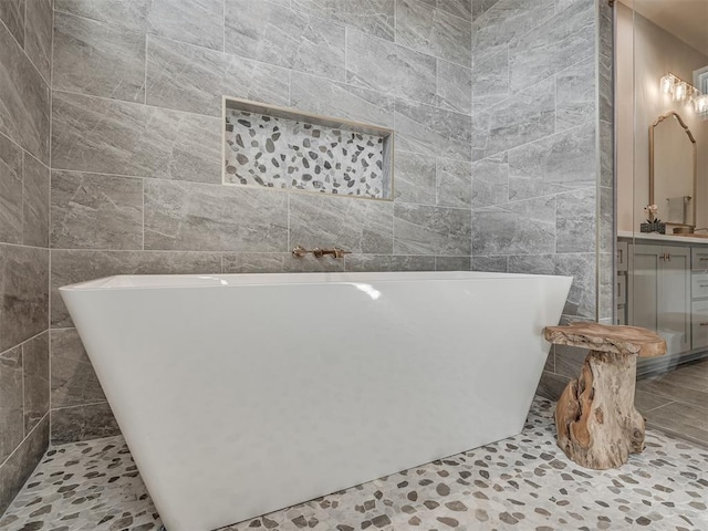 full bath with a soaking tub, tile walls, and vanity