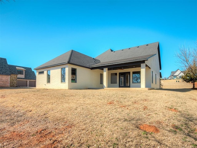 rear view of property with a patio, a lawn, and roof with shingles