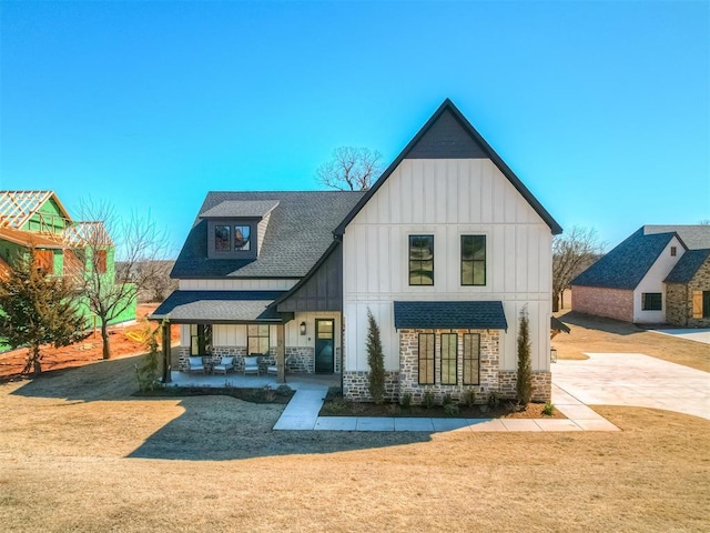 view of front of home with a front yard, a porch, a shingled roof, stone siding, and board and batten siding