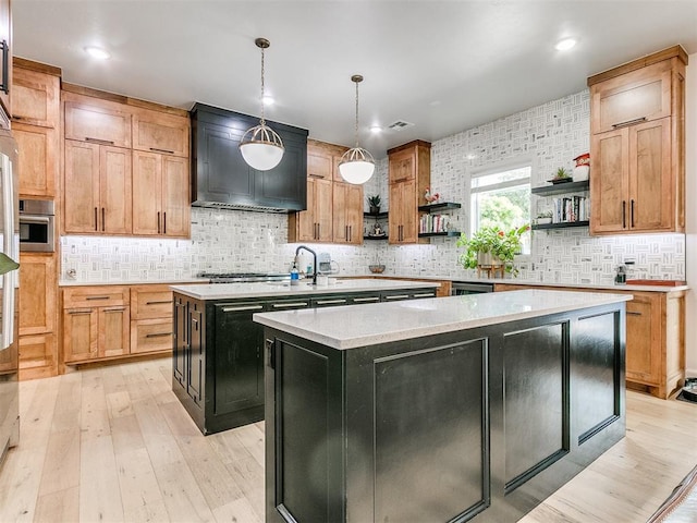 kitchen featuring decorative backsplash, a center island with sink, hanging light fixtures, and light wood-type flooring