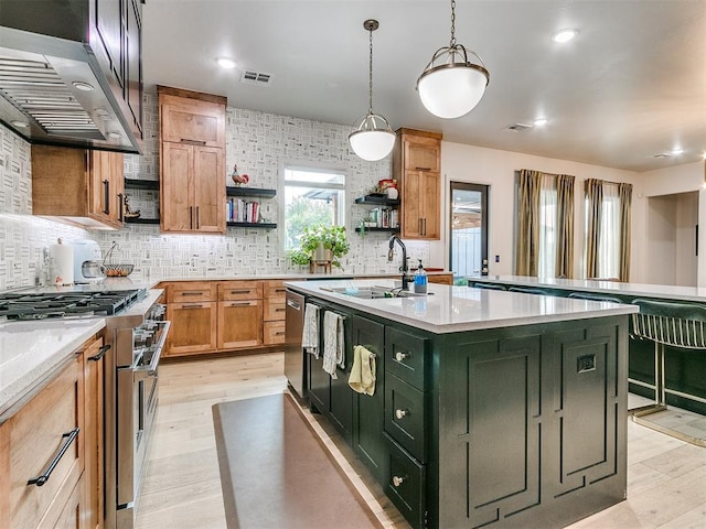 kitchen with a kitchen island with sink, wall chimney range hood, sink, light hardwood / wood-style flooring, and high end stove