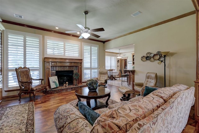 living room with ceiling fan, a fireplace, wood-type flooring, and crown molding