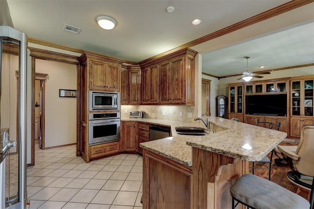 kitchen featuring kitchen peninsula, light stone countertops, a breakfast bar, stainless steel appliances, and sink